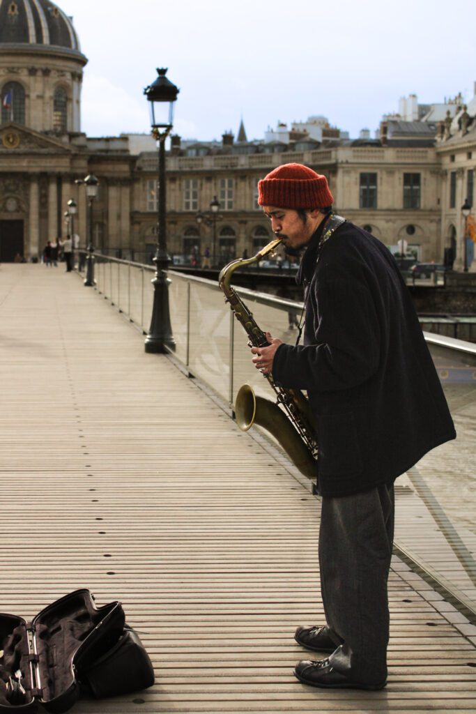 Man plays saxophone on bridge next to Louvre. 