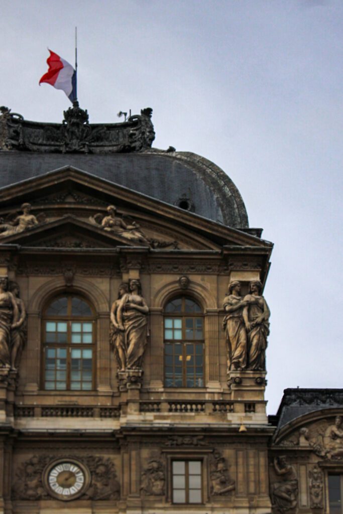 Facade of the lourve with a green roof and a grand clock against a blue skyline