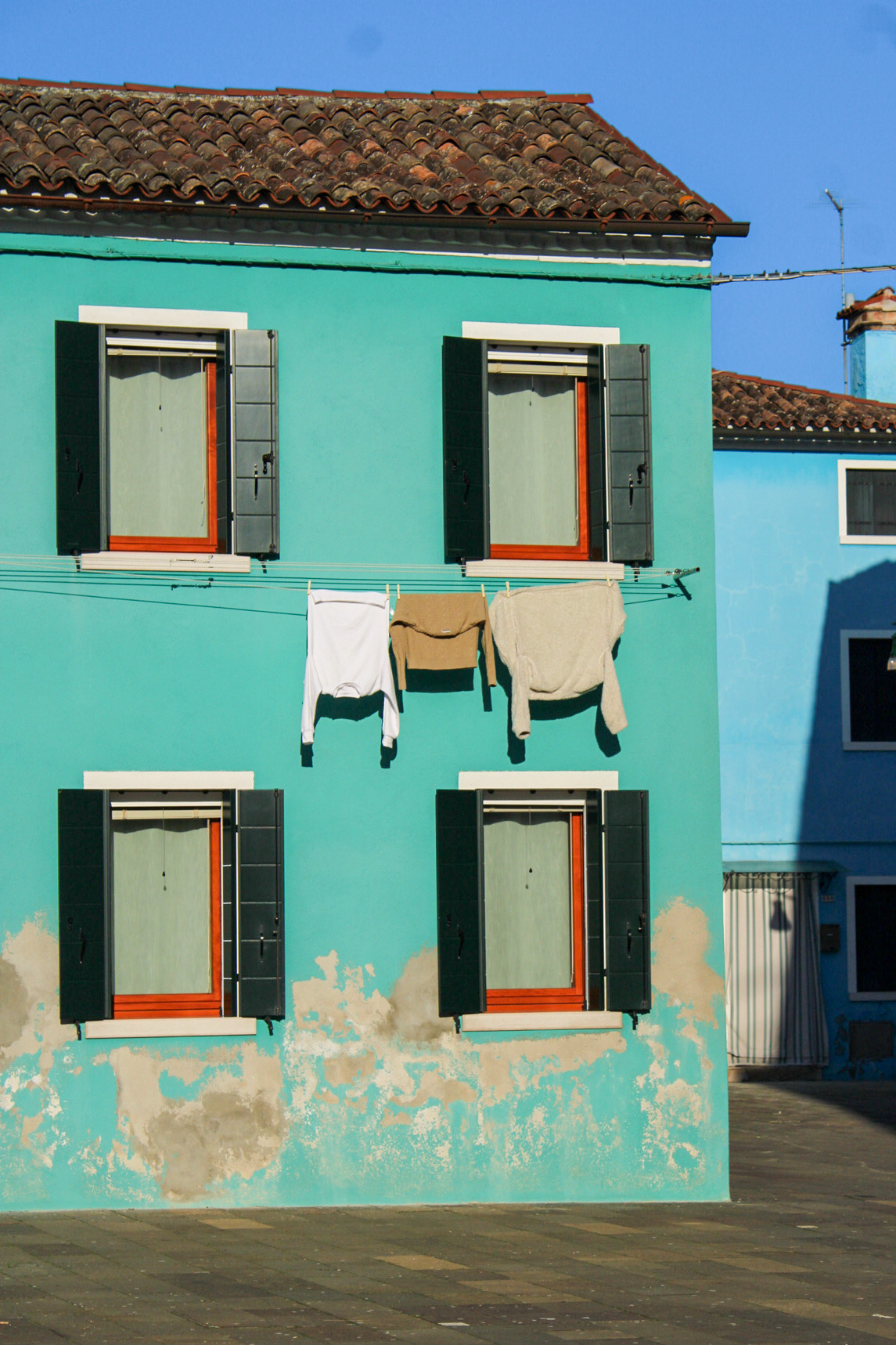 A blue facade of a house in Burano with a clothes line with clothing hanging from it.