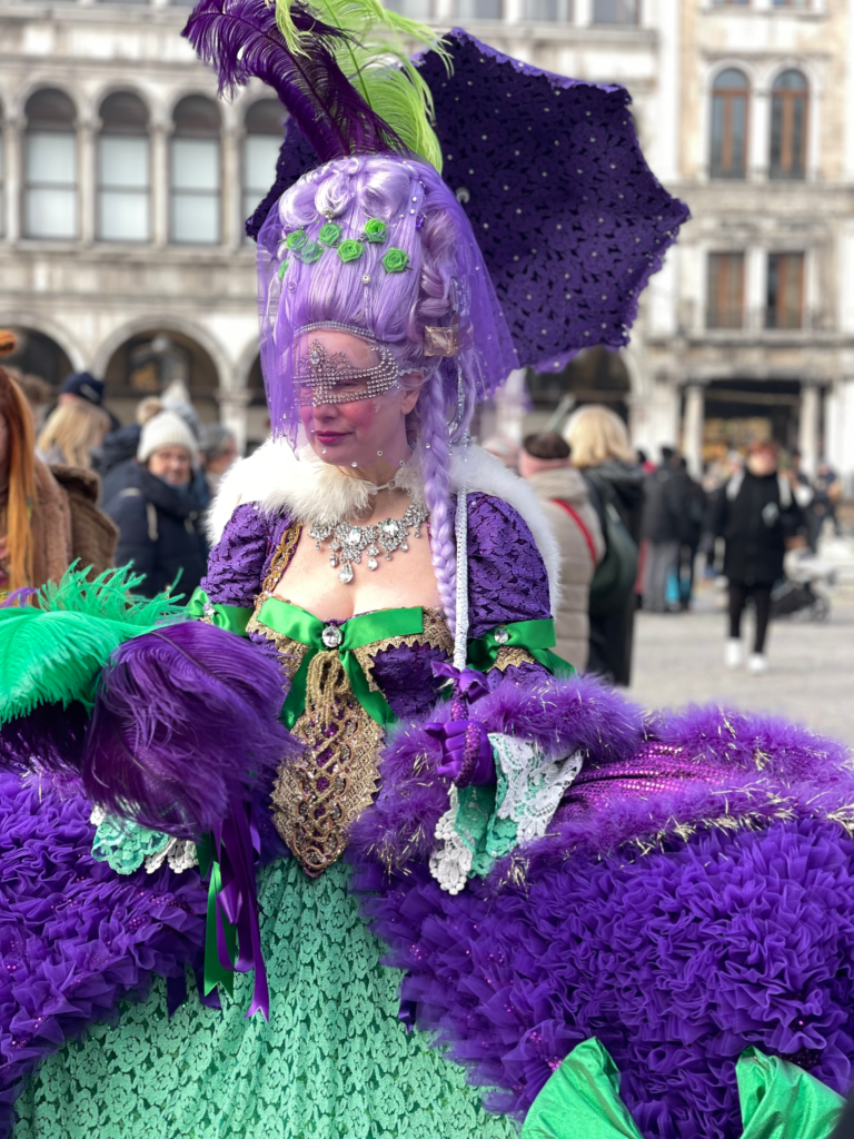 masked woman in a veil and green and purple dress in piazza san marco, venice