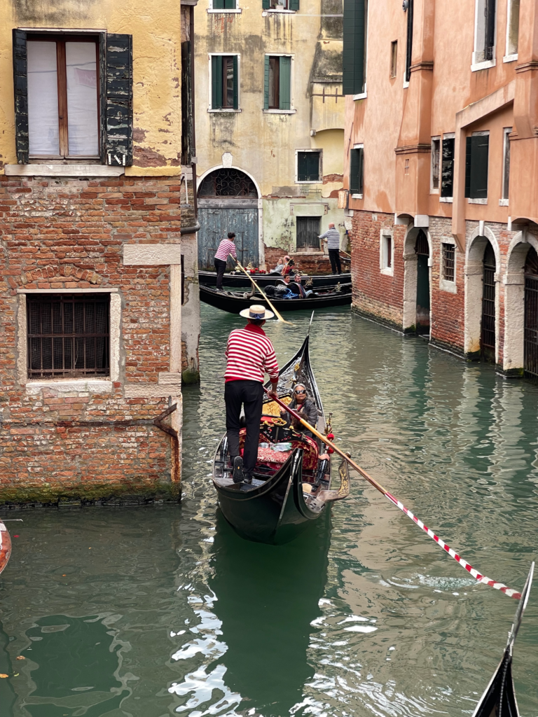 a venetian gondolier in a red and white striped shirt rows his gondola through the canals of venice, italy