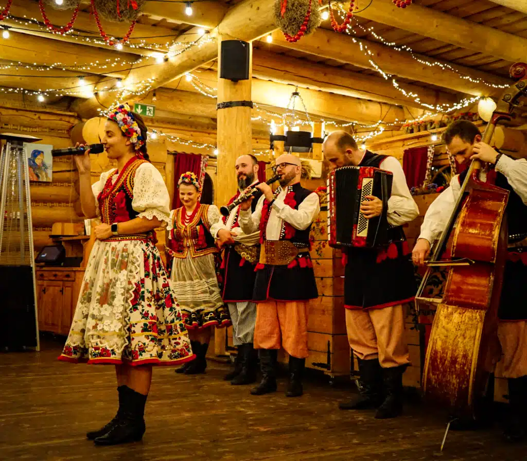 Polish folk band in traditional Kraków costumes performing with clarinet, accordion, and double bass behind a singer at a folk show in Krakow