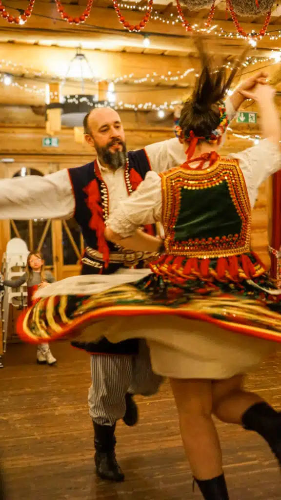 Couple in traditional Kraków folk costume spinning mid-dance at a Polish folk show, the woman's embroidered skirt flaring out in motion