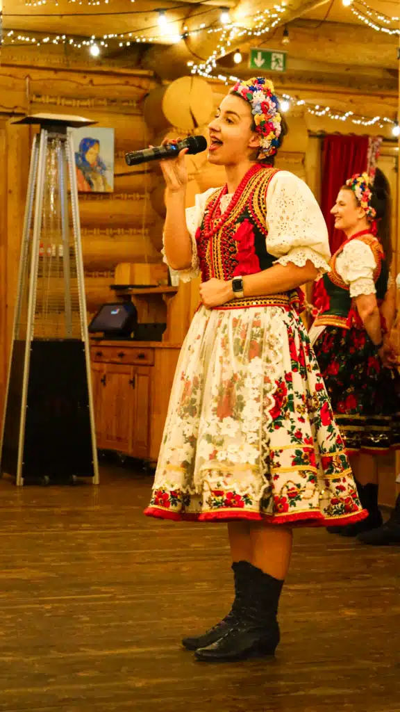 Folk singer in a traditional Kraków costume and floral wreath headpiece singing into a microphone at a Polish folk show in Krakow