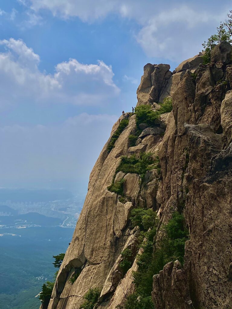 Baegundae Peak in Bukhansan National Park near Seoul Korea. Climbers are seen decending from the peak with a blue sky behind them.