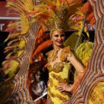 A woman participating in the Fete Du Citron Parade is posing in her costume of yellow and vibrant jewels.