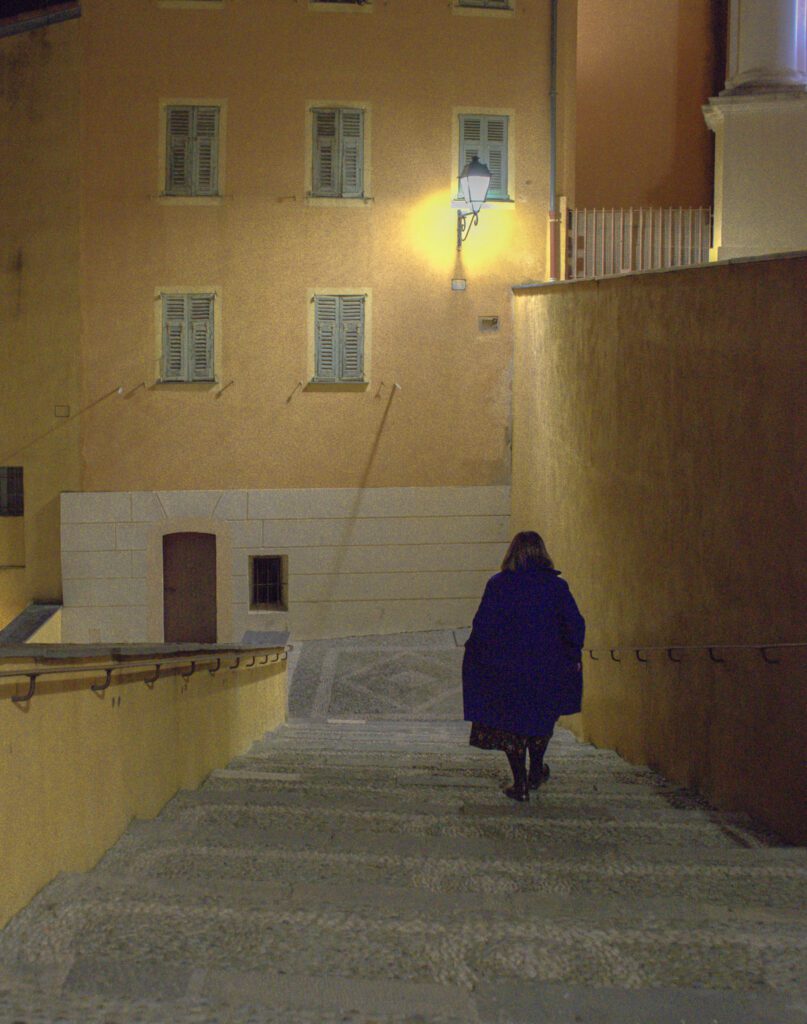 woman in long dark jacket walking down stairs in Menton, France