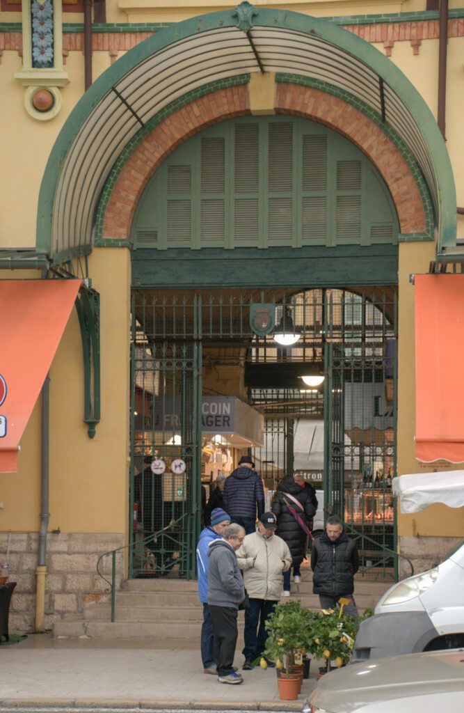 People standing outside a market in Menton. Looking at a lemon tree as cars go by
