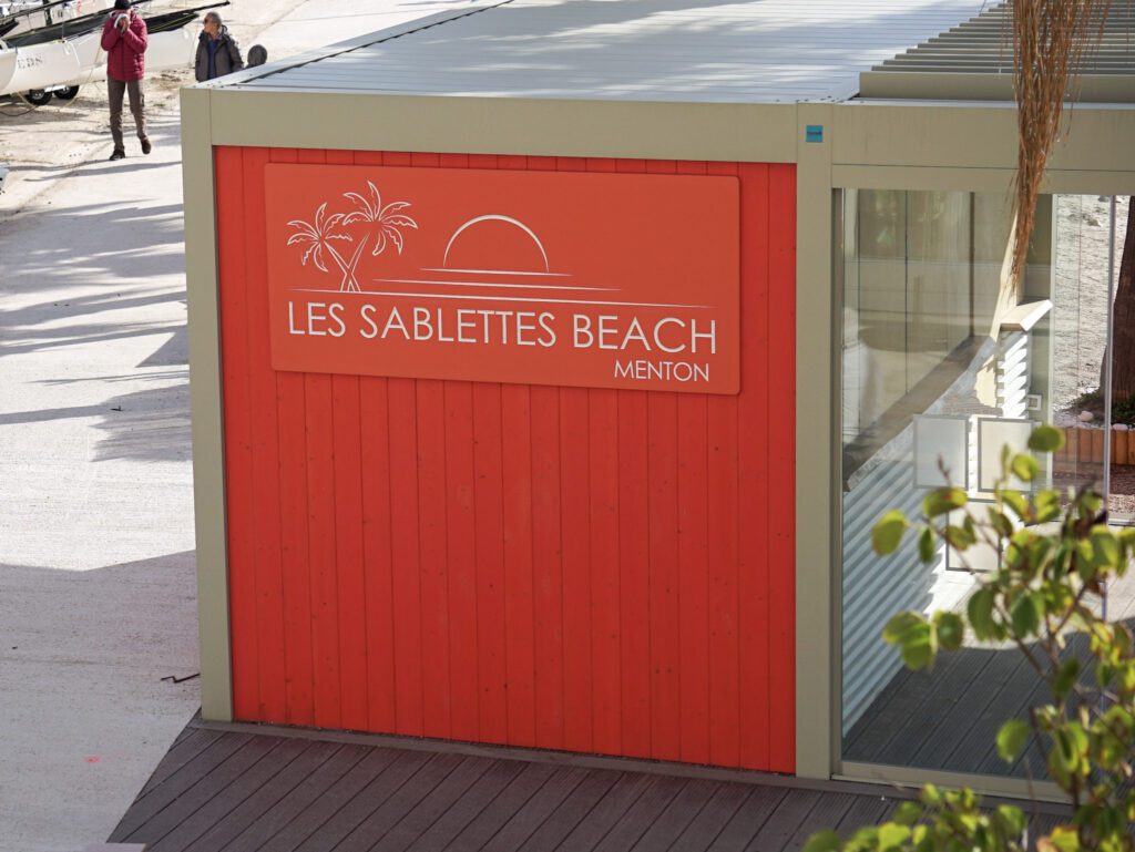 an orange wall with white writing les sablettes beach, menton