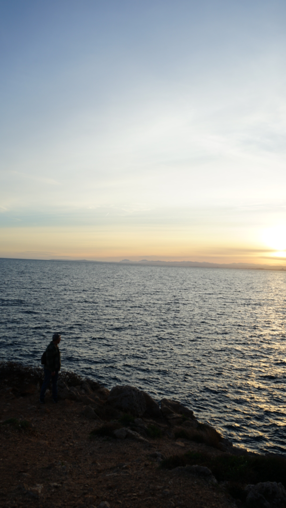 Silhouette of a person walking along the coastal trail during golden hour, with the Mediterranean shimmering under a pastel sunset sky in Villefranche-sur-Mer.