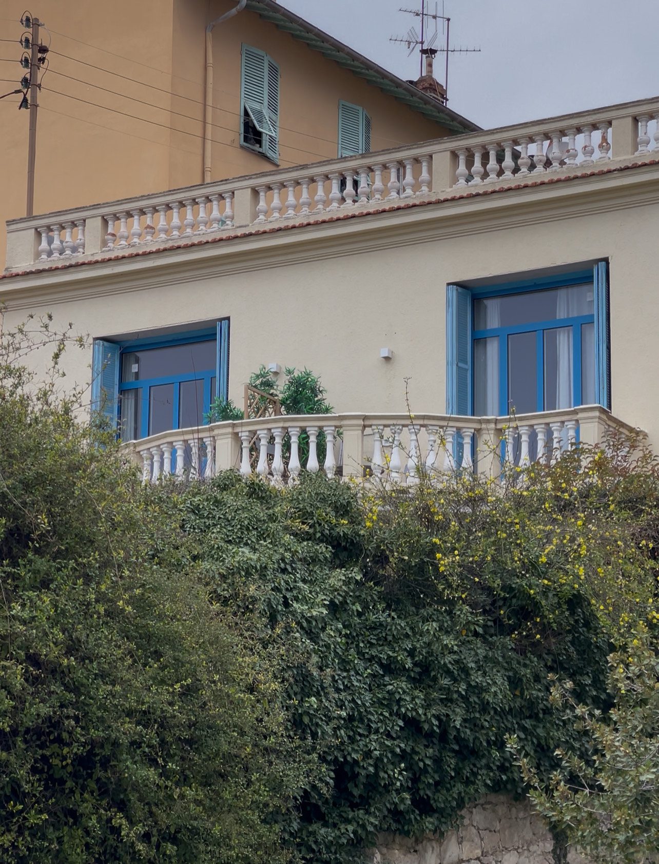 Villa with blue trim windows. Flowers and green shrubs surround it