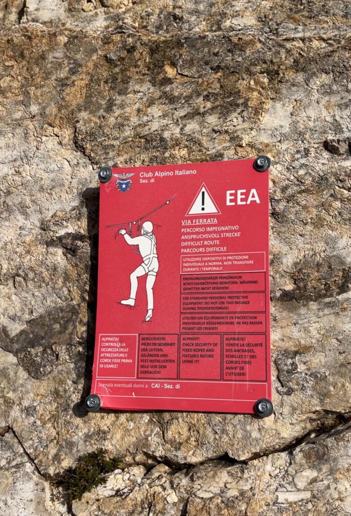 A Red Via Ferrata Caution sign posted to a rugged mountainside