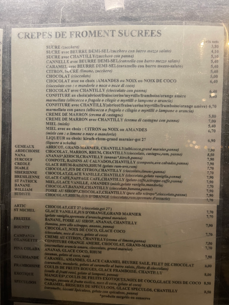 A close-up of the dessert crepe menu titled “Crêpes de Froment Sucrées” listing a variety of sweet crepes in French with Italian translations, including flavors like chocolate, caramel, and fruit preserves, with prices alongside.