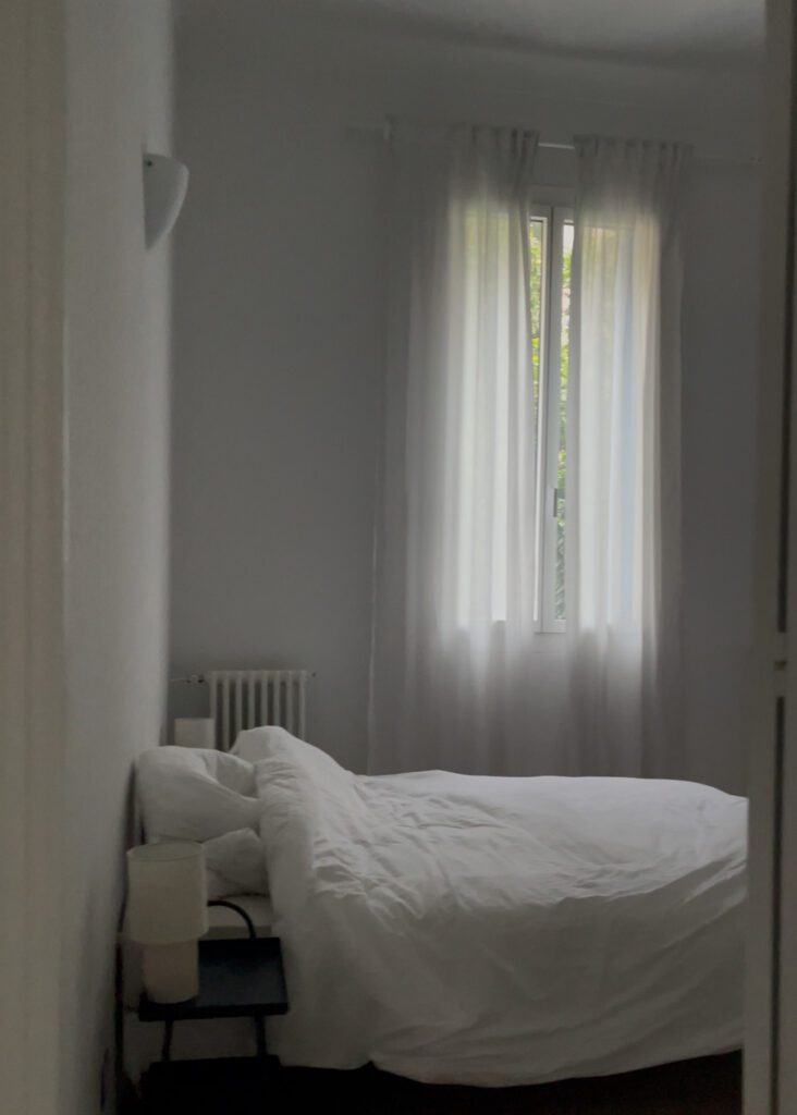 A Bed with White Sheets and white curtains in the background