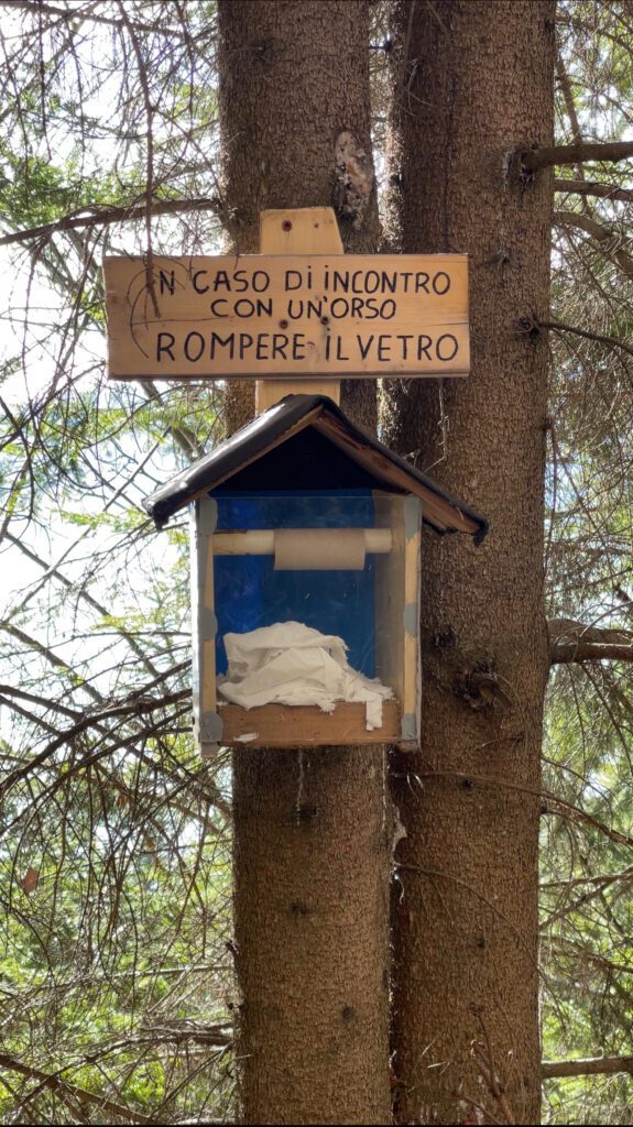 A sign in italian at the start of the Strada Delle 52 Galleries which says "In case of encounter with a bear break the glass" and theres toilet paper behind glass. 