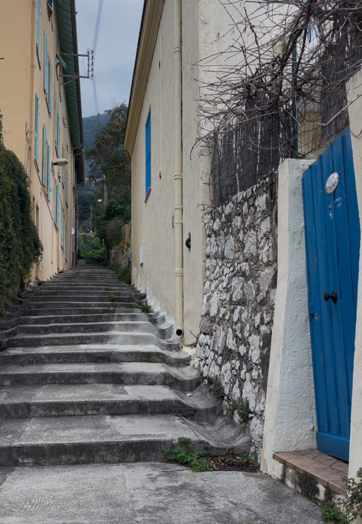 steep stairs leading up to the villa in Menton FRance. Blue door to the right and yellow buildings beyond this