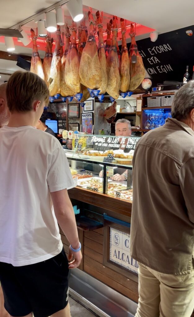 A staff member of Bar Casa Alcalda looks on as he serves hungry patrons. There is a glass case filled with Pintxos, both cold and warm.