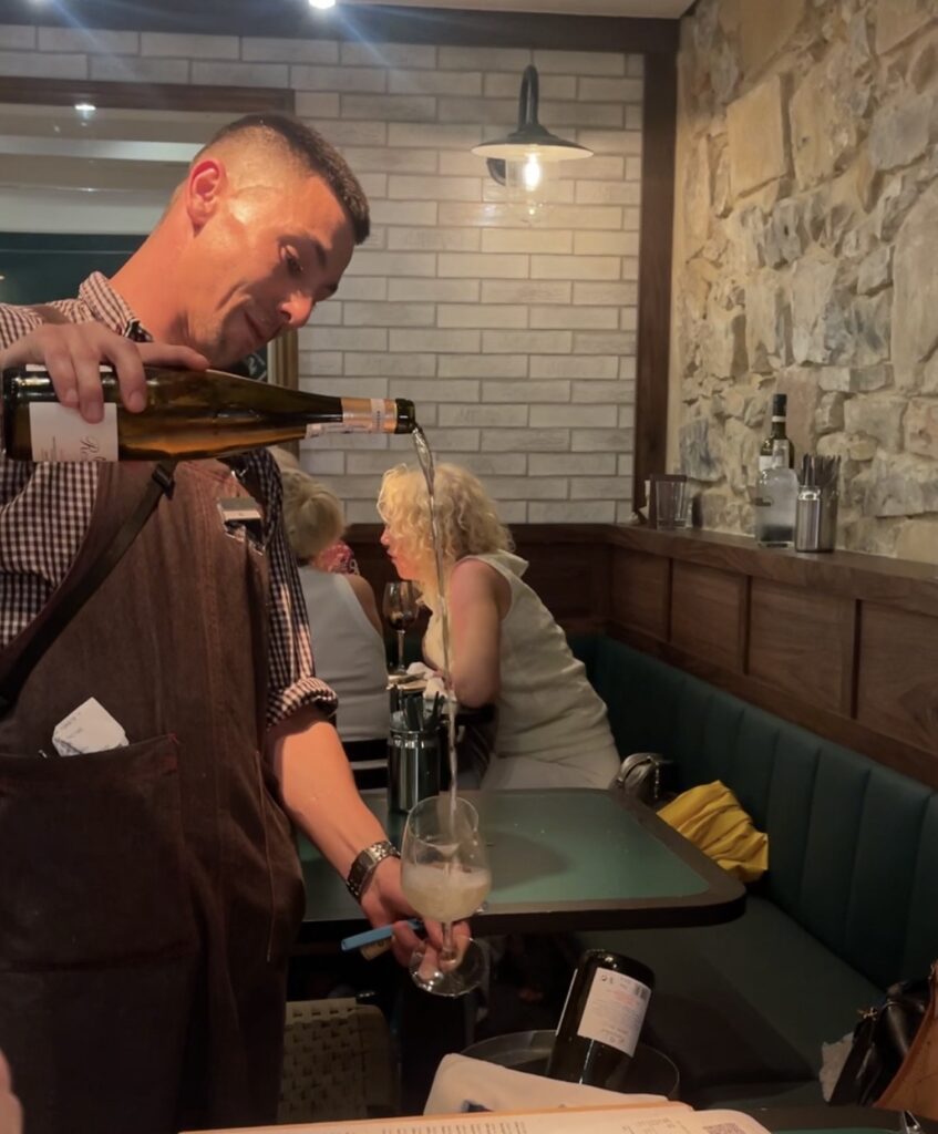 A Man practices what is called a Basque Long Pour of cider into a glass at a bar in San Sebastian