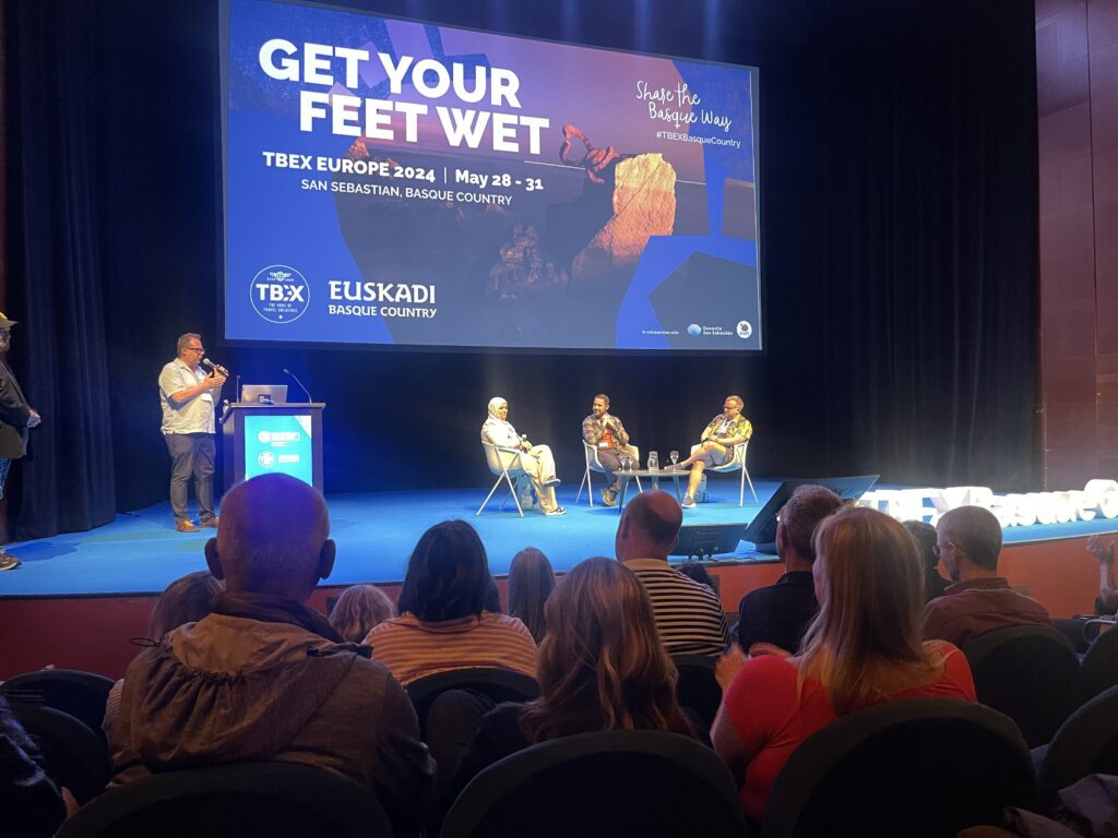 TBEX Closing Keynote with speakers at a roundtable and a moderator on stage.