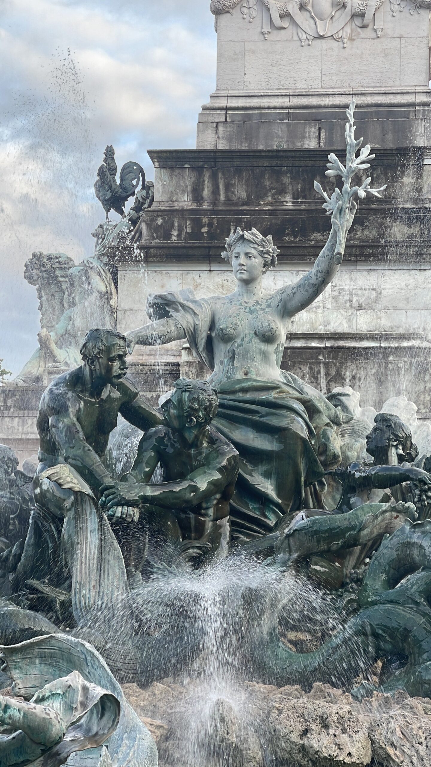 The Fontaine du Char du Triomphe de la Concorde features a statue seated on a throne, partially draped, with a bare torso like Truth. In her hand, she holds an olive branch (a symbol of peace) and extends her protective arm. The fountain celebrates the triumph of Concord and Peace. Nearby, a man, a woman, and a child ride a fish—a representation of family happiness resulting from concord and peace. The fountain also includes sculptures depicting commerce, industry, arts, and sciences. Two large shells are pulled by seahorse-like horses, adorned with reeds, fish, and frogs.