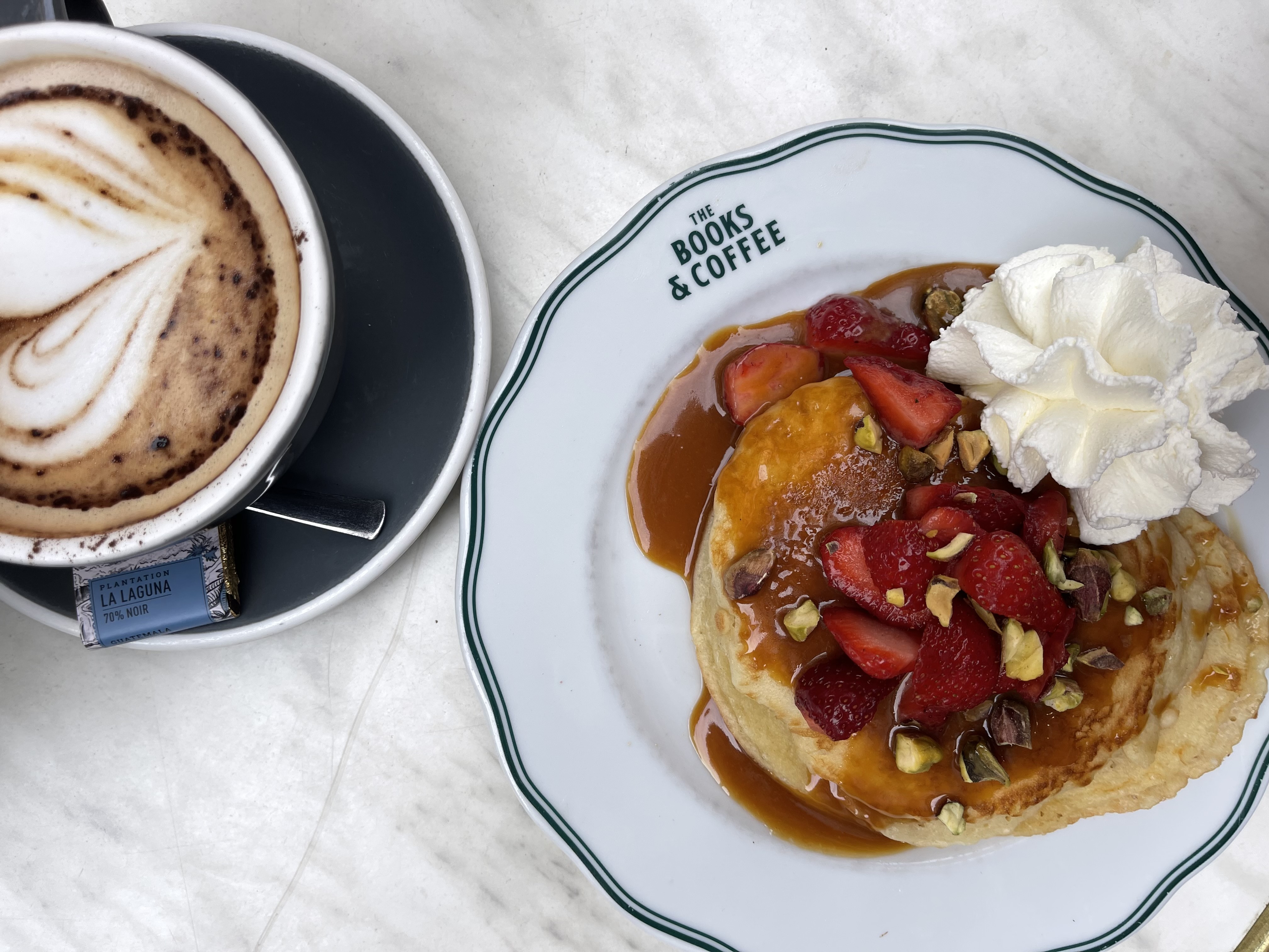 Scrumptious plate of pancakes topped with fresh strawberries, pistachios, caramel sauce, and whipped cream, served alongside a steaming cup of coffee. These delightful pancakes are from Books and Coffee in Bordeaux, France.