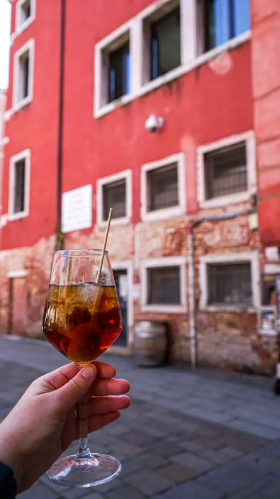 A hand holding up a cynar spritz in a piazza on one of the best tours of venice
