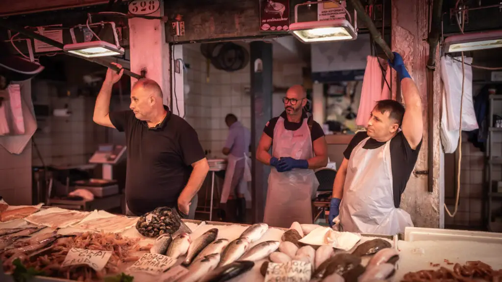 Three men stand by their seafood table in the Rialto Market selling fish