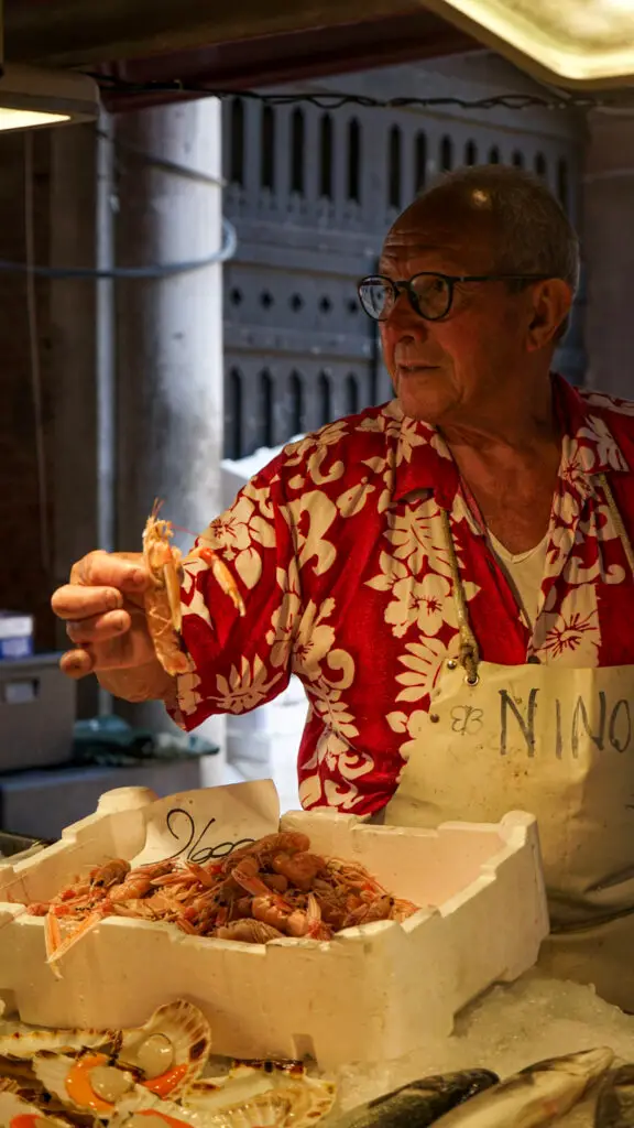 a fishmonger displays scampi in his hands as he looks on a passerbys during one of the best tours in venice