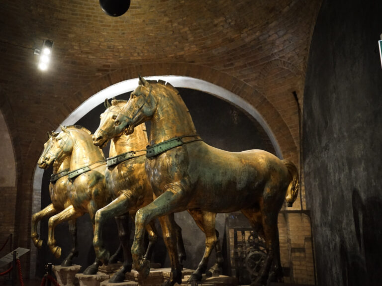 Bronze statues of horses in St. Marks Basilica set in a brick room with lights shining down on them
