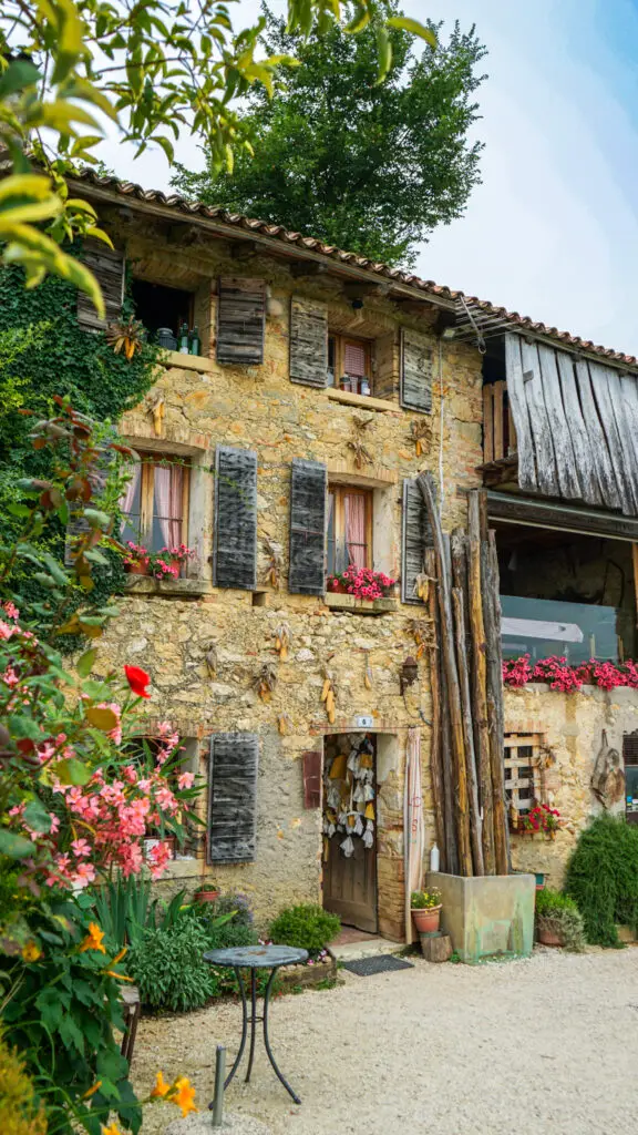 Front Facade of Osteria Senz Oste. Wild flowers grow on a bush beside the building with a table in front.