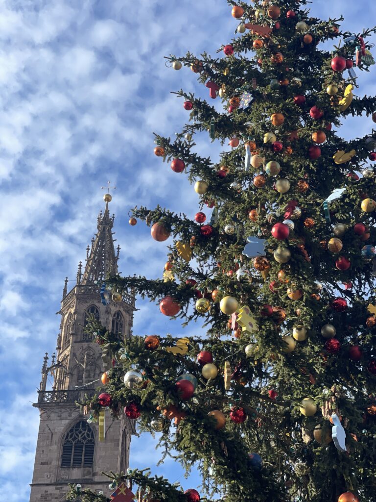 View of a christmas tree with red baubles on it and a church steeple with blue skies