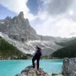 Woman standing on a rock in front of a lake in the mountains.