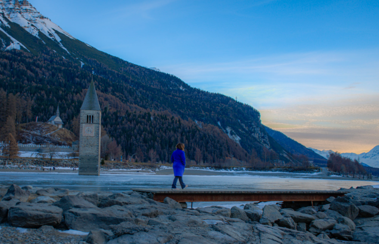 Walking across the frozen Lago di Resia toward the sunken Curon bell tower in the Dolomites, South Tyrol in winter