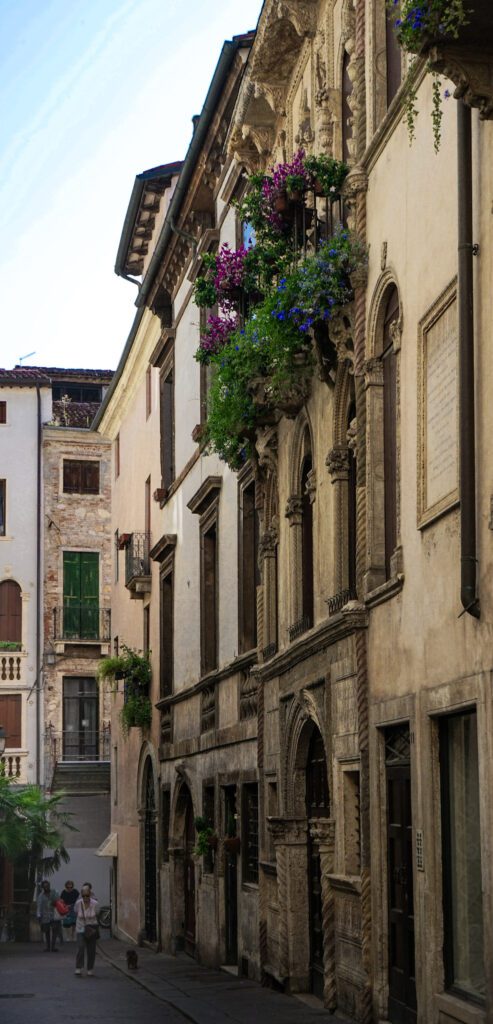 Street in Vicenza, Italy with flowers overflowing on a balcony as a woman walks by