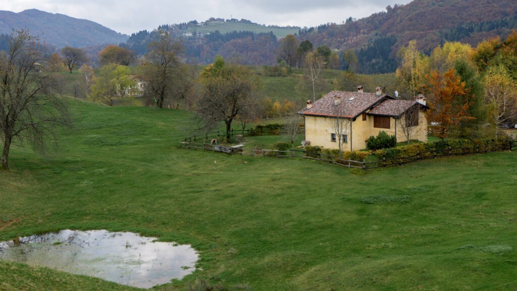 Sentiero Grandi Alberi starting point, a house sits in a valley with a pond.