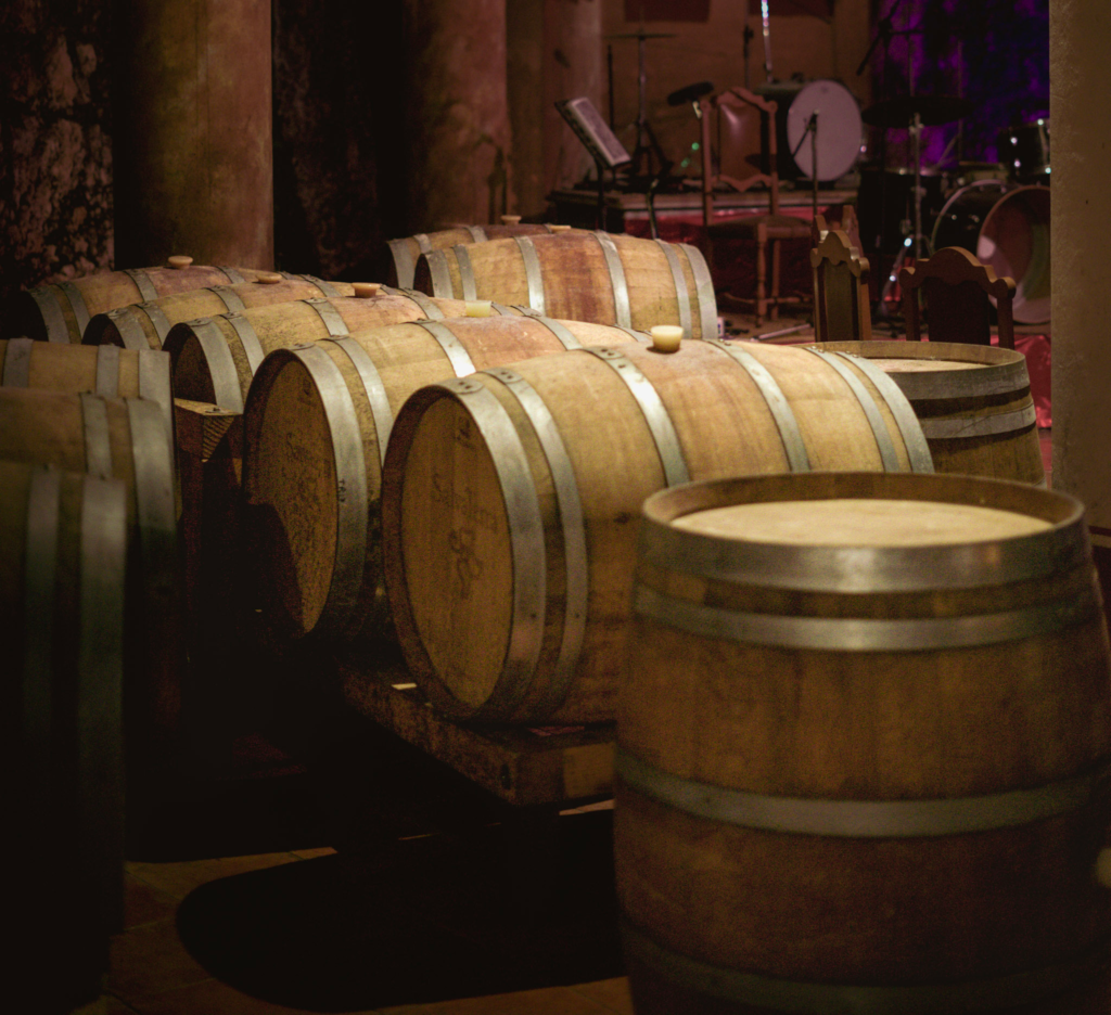 Rows of oak wine barrels rest in a dimly lit aging cellar at Ca’ Bruzzo, with musical instruments in the background suggesting live events or tours.