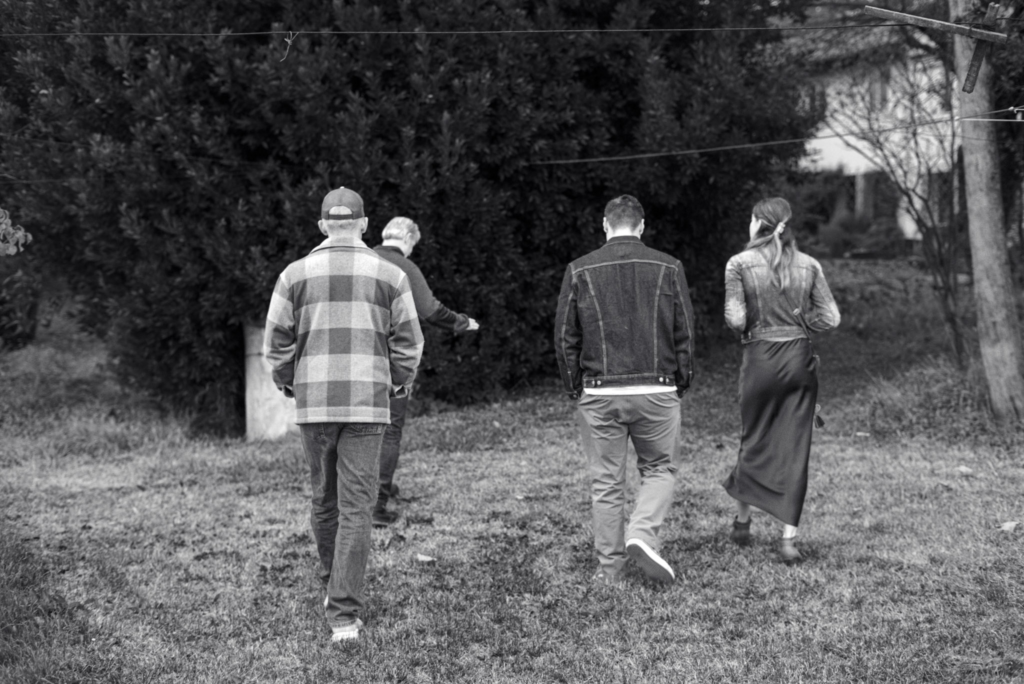 Four people walking away from the camera across the grassy grounds of Ca’ Bruzzo, heading toward dense trees, evoking a relaxed winery tour experience Things to do in Vincenza