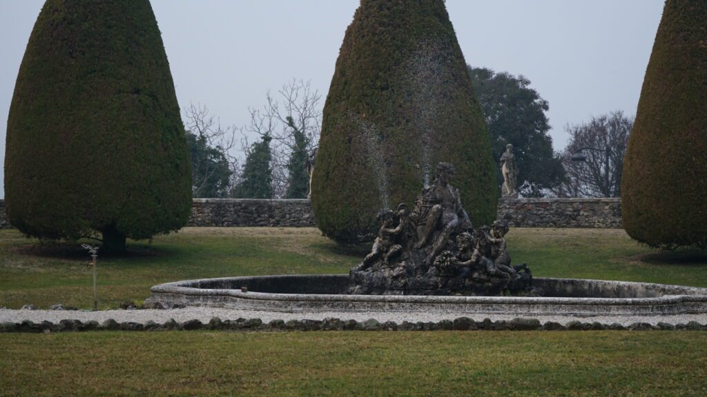 An ornate fountain on the grounds of Villa Godi Malinverni feautring sculptures in different positions set on a green lawn