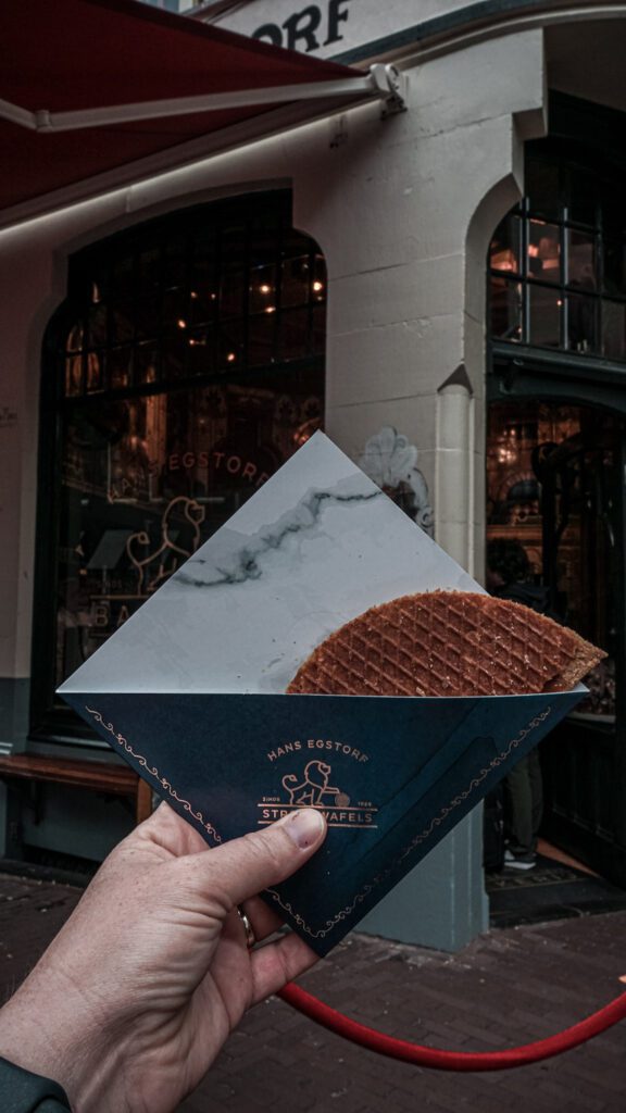 A female hand holding a stroopwaffle in a piece of paper up against a brick wall