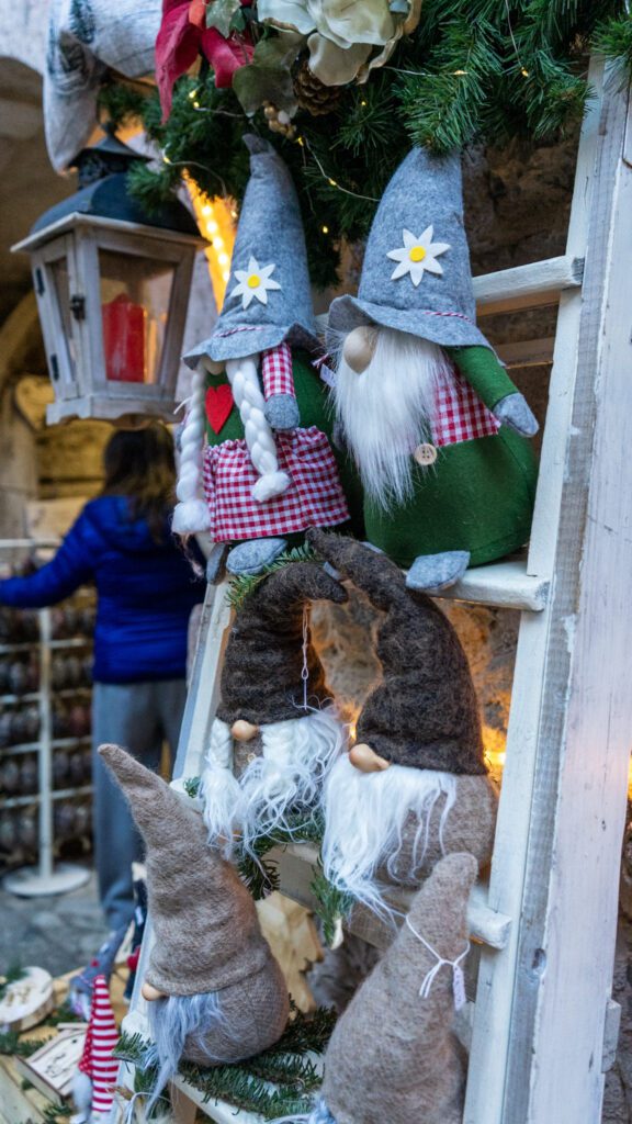 Stuffed Gnomes in colorful outfits and grey hats sitting on a wooden ladder at Rango Christmas Market.