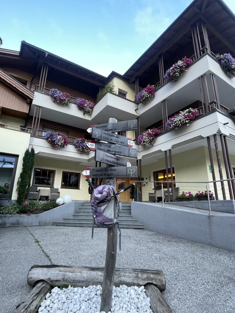 Front of Hotel Trenker with balconies full of purple and pink flowers and a signpost that showcases hikes near by