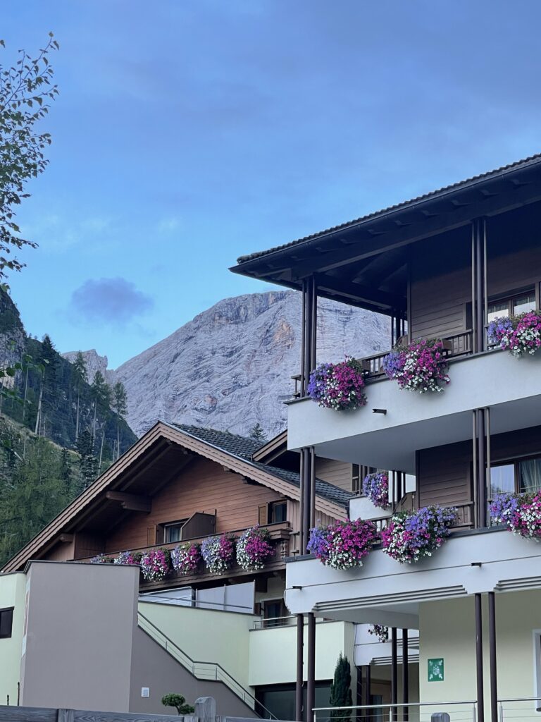 Front of Hotel decorated with pretty pink and purple flowers with dolomiti mountain rising in the background