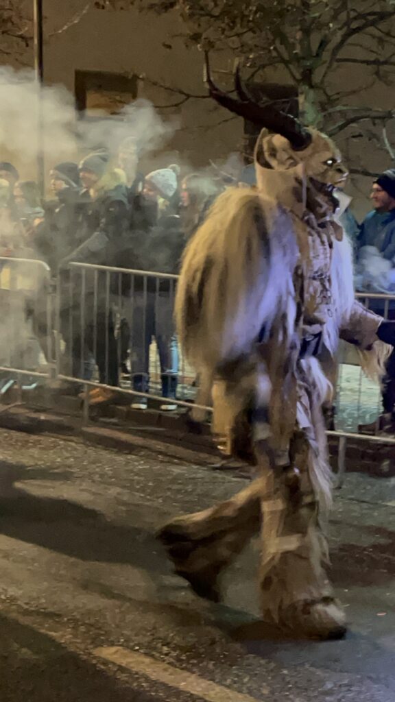 A furry white krampus walks ominously towards the crowd