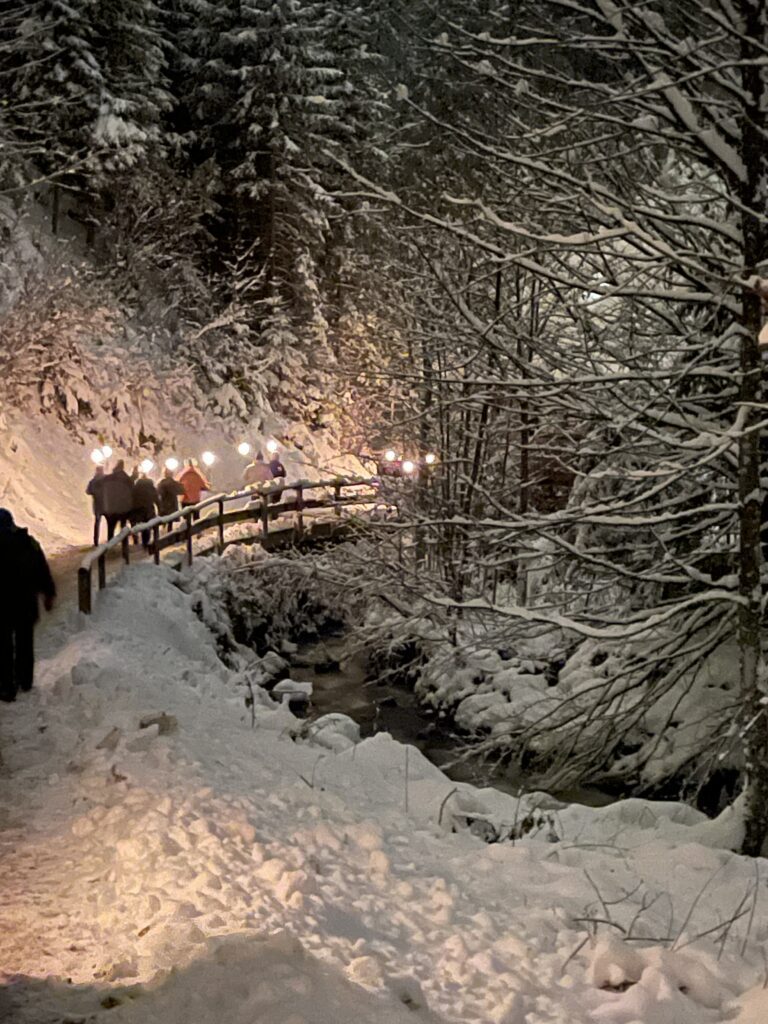 People walking on a snowy path during the Ravenna Gorge Christmas Market. The path is all lit up by torchlit glow