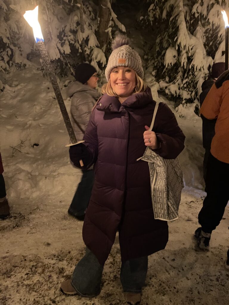 Woman holding a torch walking along a snowy path with a group of people in jackets and hats