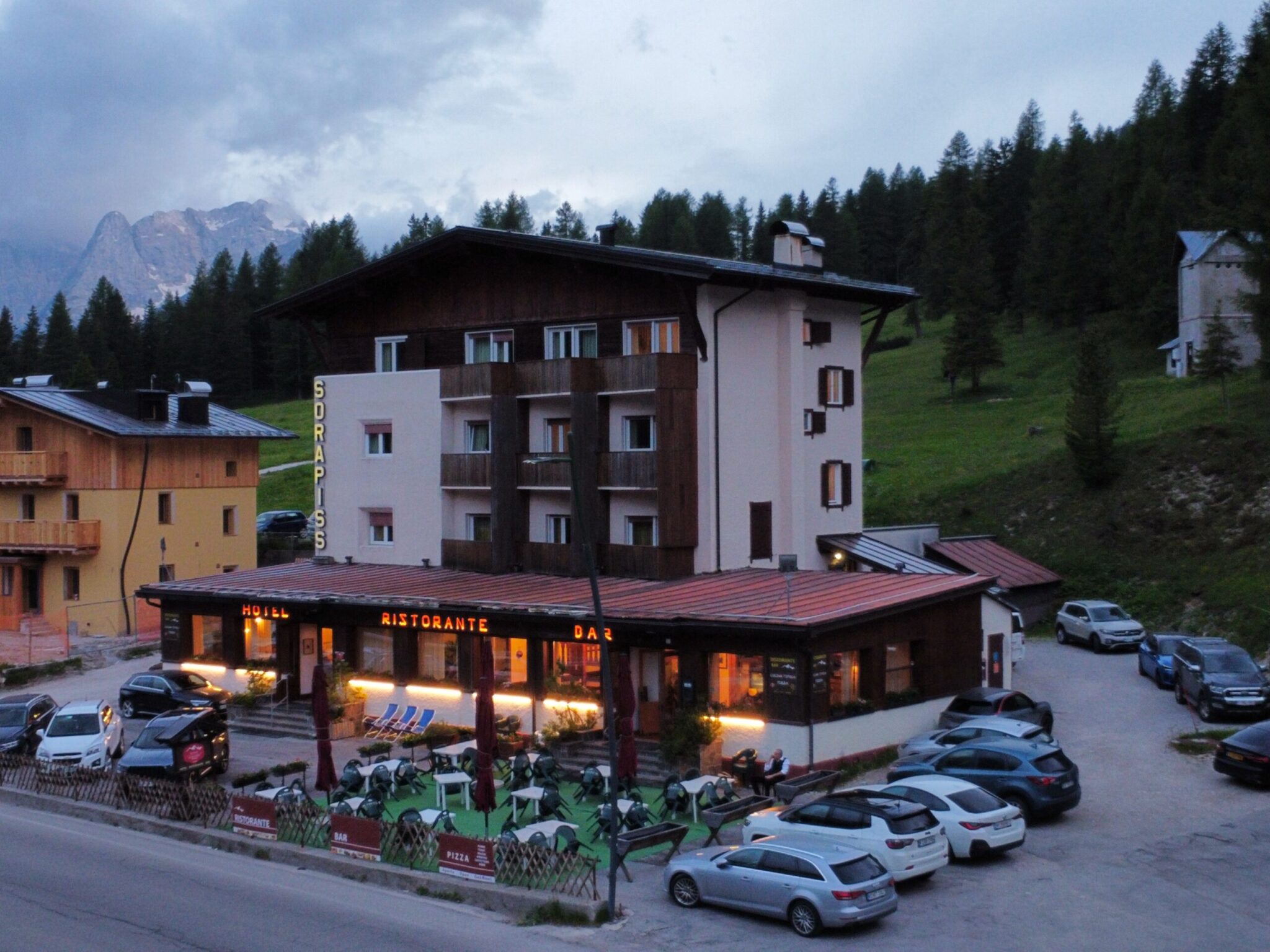 Facade of Sorapis Hotel with lights shining and cars surrounding it.
