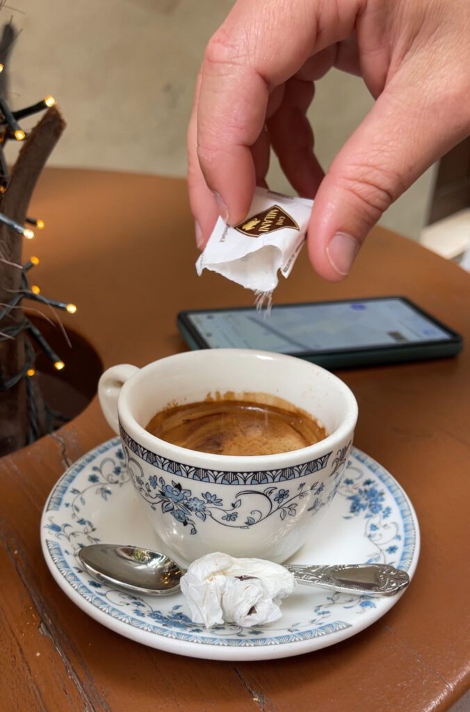 Coffee served in ornate china at Cafe Pigafetta in Vicenza Italy as a hand appears to pour more sugar in the cup.