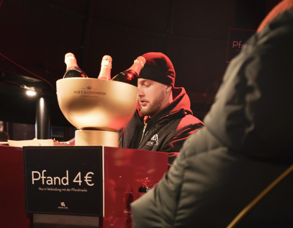 Man pouring champagne with a sign that reads Pfand 4Euro which is a deposit in germany. 