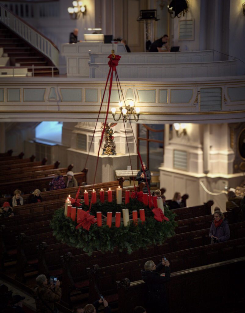 Advent wreath hanging from the ceiling of the church, with red and white candles. 7 are lit. 