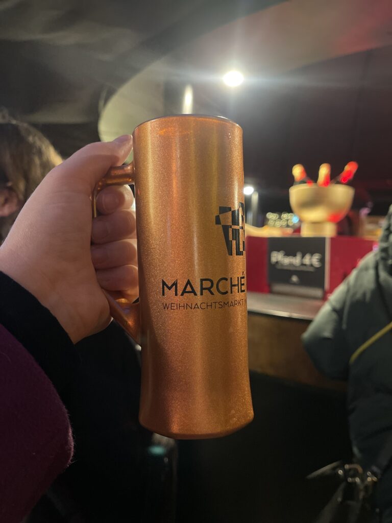 Arm holding up the Marche De Noel Christmas Market mug that is copper with black writing 